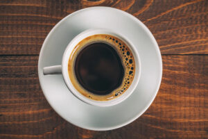 Tazza di caffè gourmet nero su un tavolo di legno, vista dall'alto, con un bordo cremoso che ne evidenzia la ricchezza e qualità