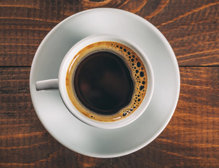 Tazza di caffè gourmet nero su un tavolo di legno, vista dall'alto, con un bordo cremoso che ne evidenzia la ricchezza e qualità